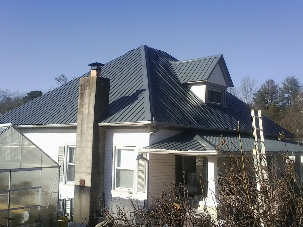 Dark blue standing seam metal roof on a white farmhouse with dormer — Slate & Tile Roof Repair by Roofing Brothers in Saint Martinville