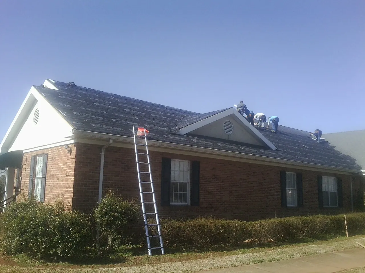 Crew tearing shingles off a brick ranch roof with a ladder set — Metal Roof Repair work by our crew in Saint Martinville