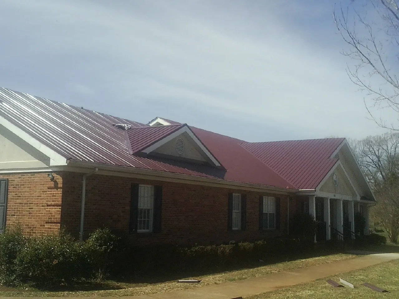 Red metal roof with gabled entries on a long brick building, from a Hail Damage Roof Repair job in Saint Martinville