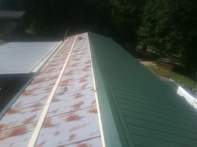 Old rusted panels beside newly installed green metal roofing — Wind Damage Roof Repair by Roofing Brothers in Saint Martinville