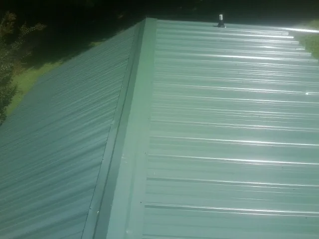 New green metal panels meeting at the ridge of a roof — Flat Roof Repair work by our crew in Saint Martinville