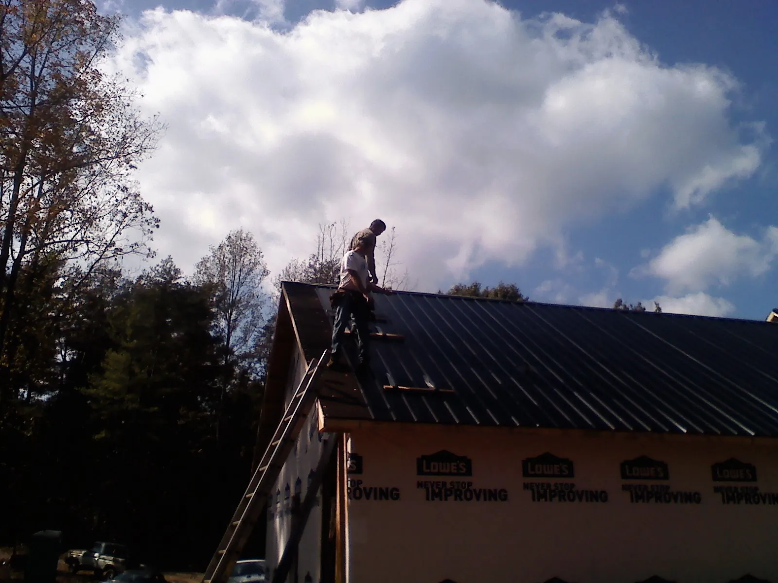 Roofer fastening dark metal panels high against a cloudy sky, from a Roof Inspection job in Saint Martinville