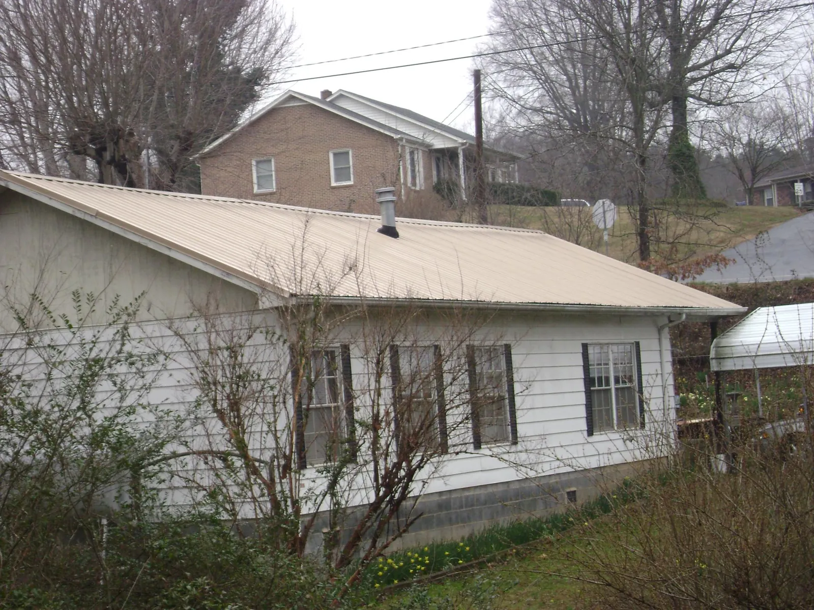 Tan metal roof on a white sided house set into a hillside — Commercial Roofing by Roofing Brothers in Saint Martinville