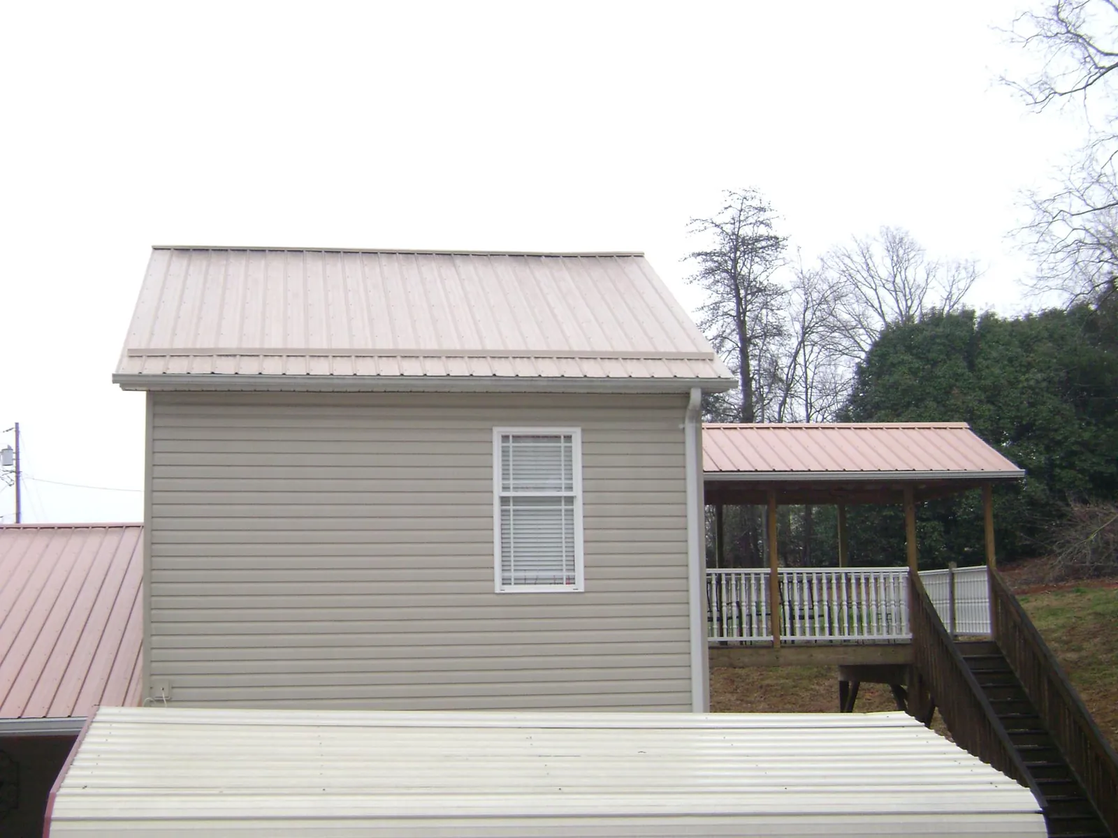 Tan metal roofs on a two story addition and attached porch, from a Roof Replacement job in Saint Martinville